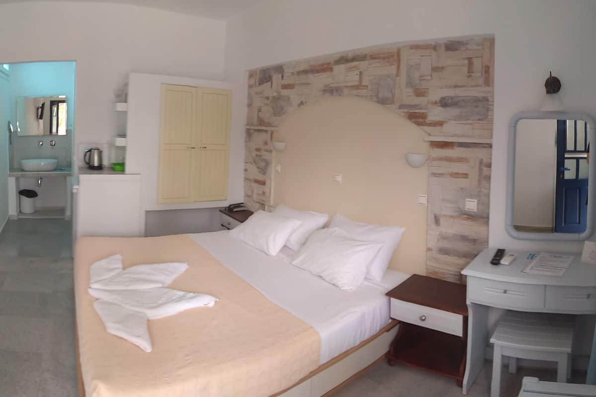 A hotel room with a bed, a bedside table, a mirror, a wardrobe, and a bathroom visible in the background.