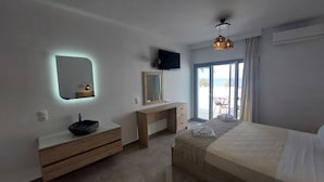 Un dormitorio con cama, un escritorio de madera, un espejo, un televisor en la pared y vistas al exterior.