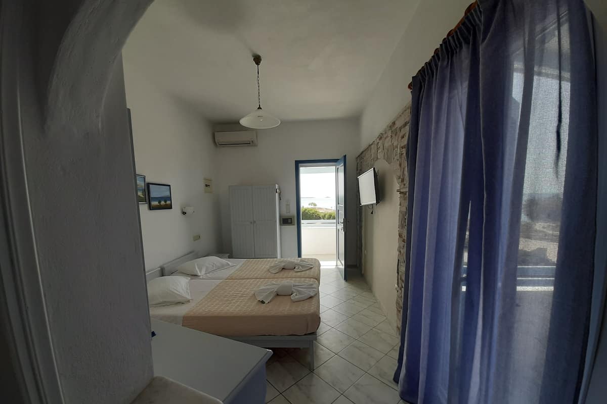A hotel room with two beds, a desk, a wardrobe, a TV, and a view of the outdoors.