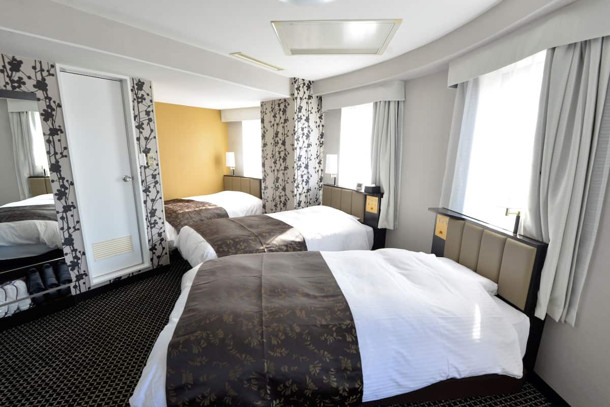 A hotel room with two beds, a wardrobe, a bathroom, and a large window with curtains.