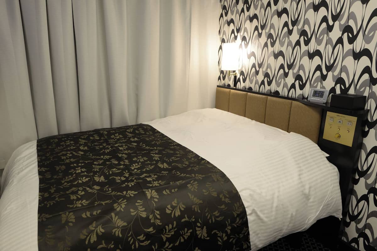 A hotel room with a bed, curtains, a TV, a wall clock, and a control panel.