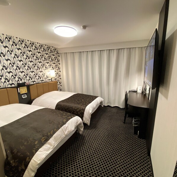 A hotel room with two beds, a desk, a television, and a patterned wall.