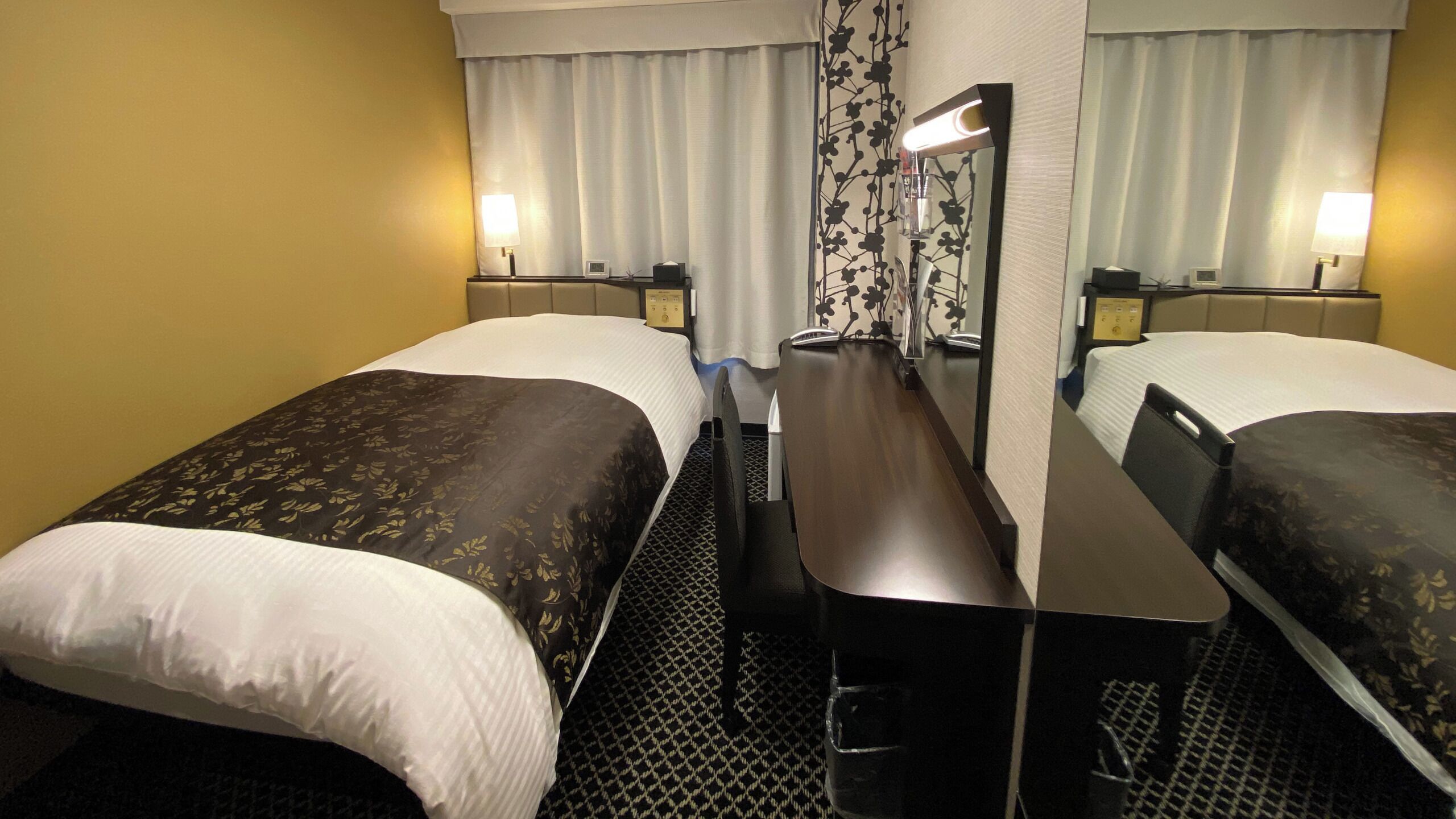 Habitación de hotel con dos camas, un escritorio, un espejo y una ventana con cortinas.