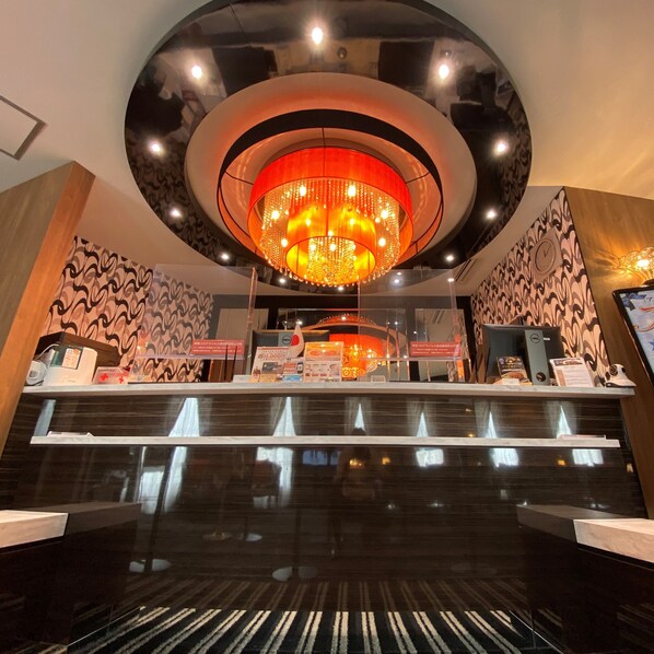 Zona de recepción de un hotel con un candelabro moderno, un mostrador de recepción y paredes con diseño.
