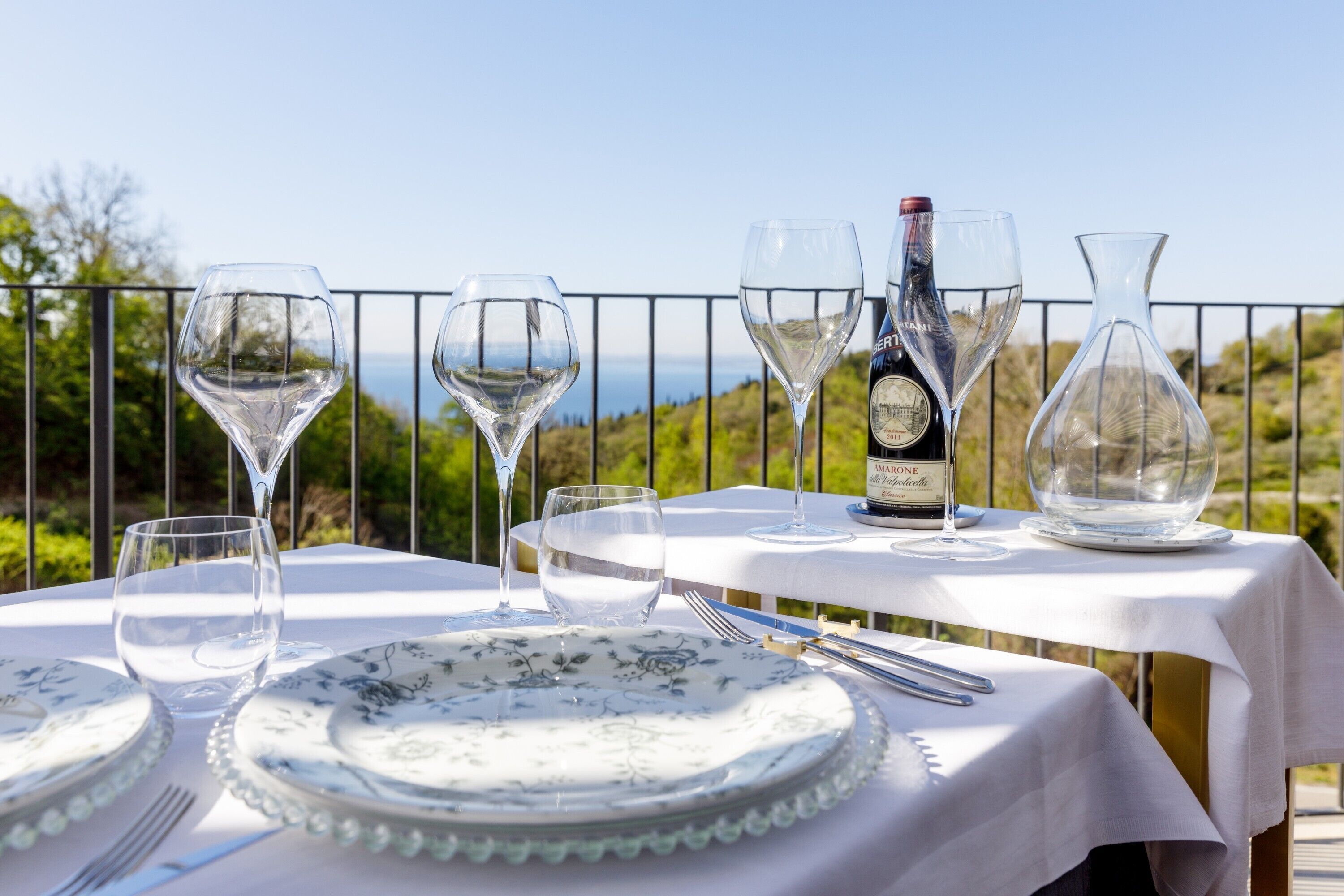 A table set for dining with wine glasses, a bottle of wine, and a water glass, overlooking a scenic landscape.