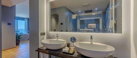 Un baño moderno con dos lavamanos grandes de color blanco, un espejo amplio y vistas al balcón.
