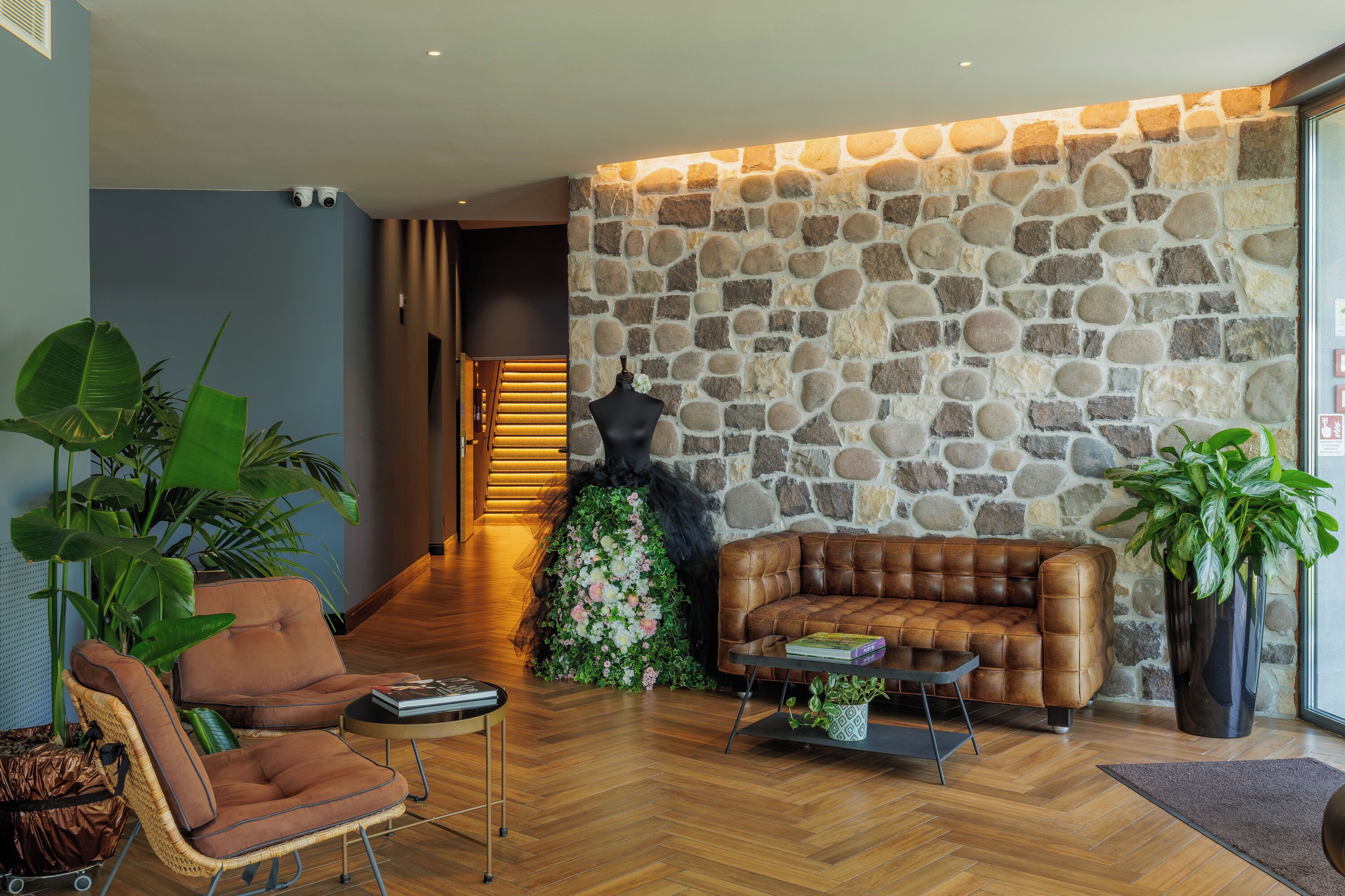 A modern living room with a stone accent wall, leather sofa, and large green plants.