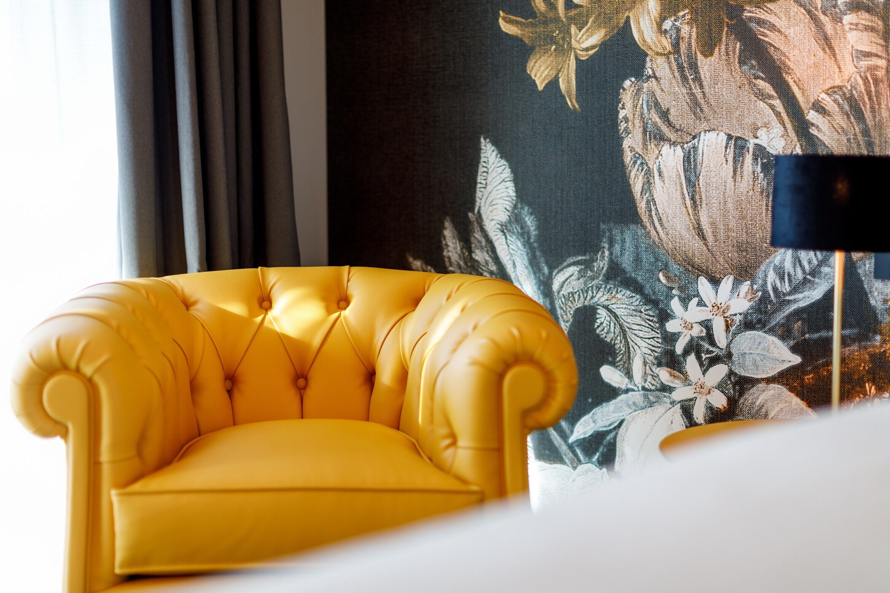 A yellow armchair in a room with a floral tapestry and a black floor lamp.