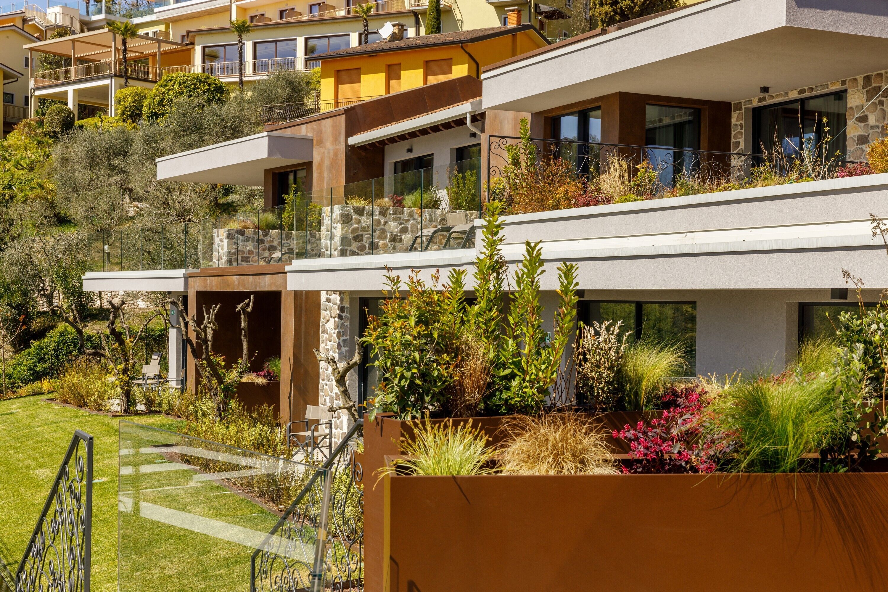 A modern multi-story residential building with balconies, stone walls, and lush landscaping.