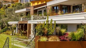A modern multi-story residential building with balconies, stone walls, and lush landscaping.