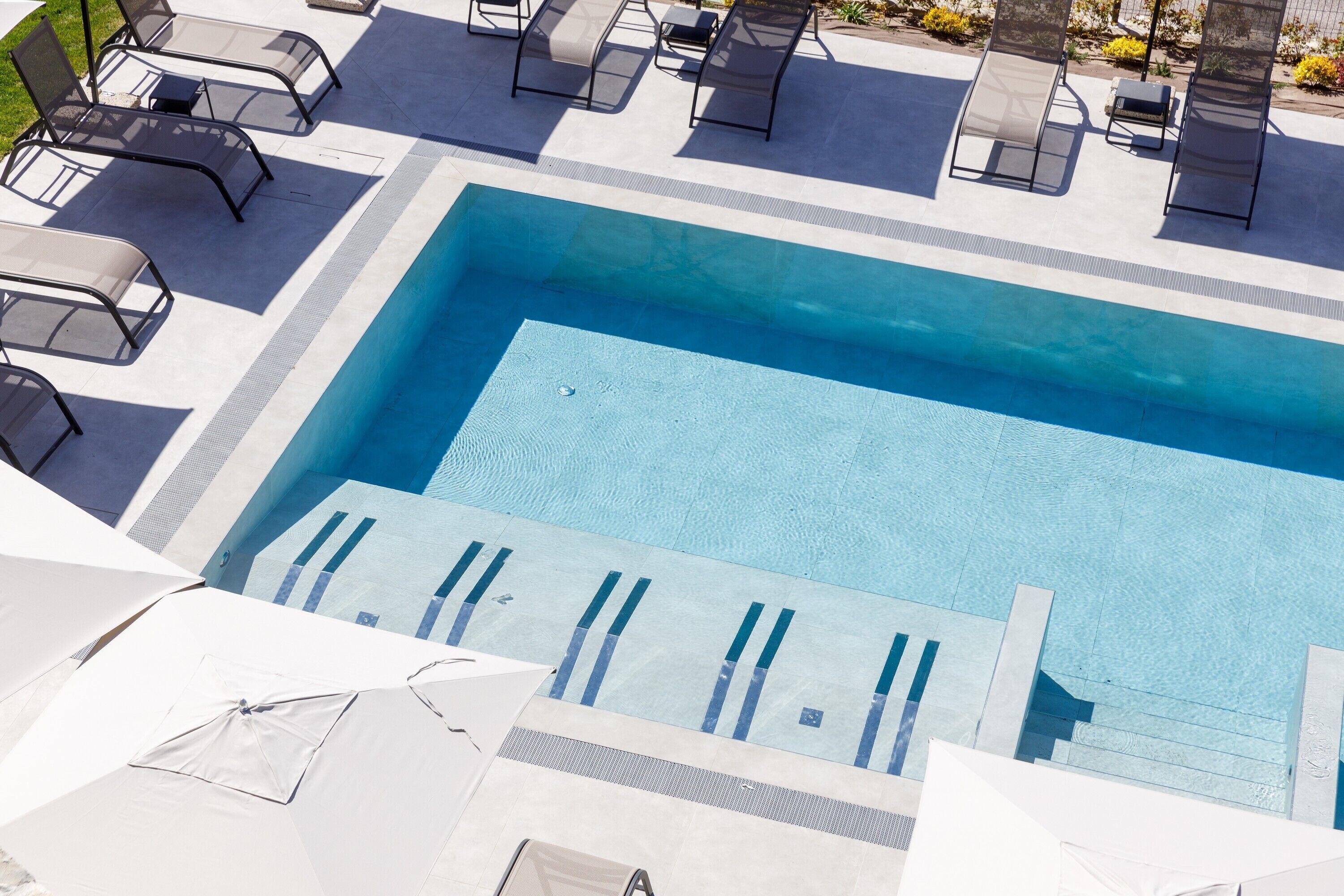 A rectangular swimming pool with clear blue water, surrounded by lounge chairs and umbrellas.