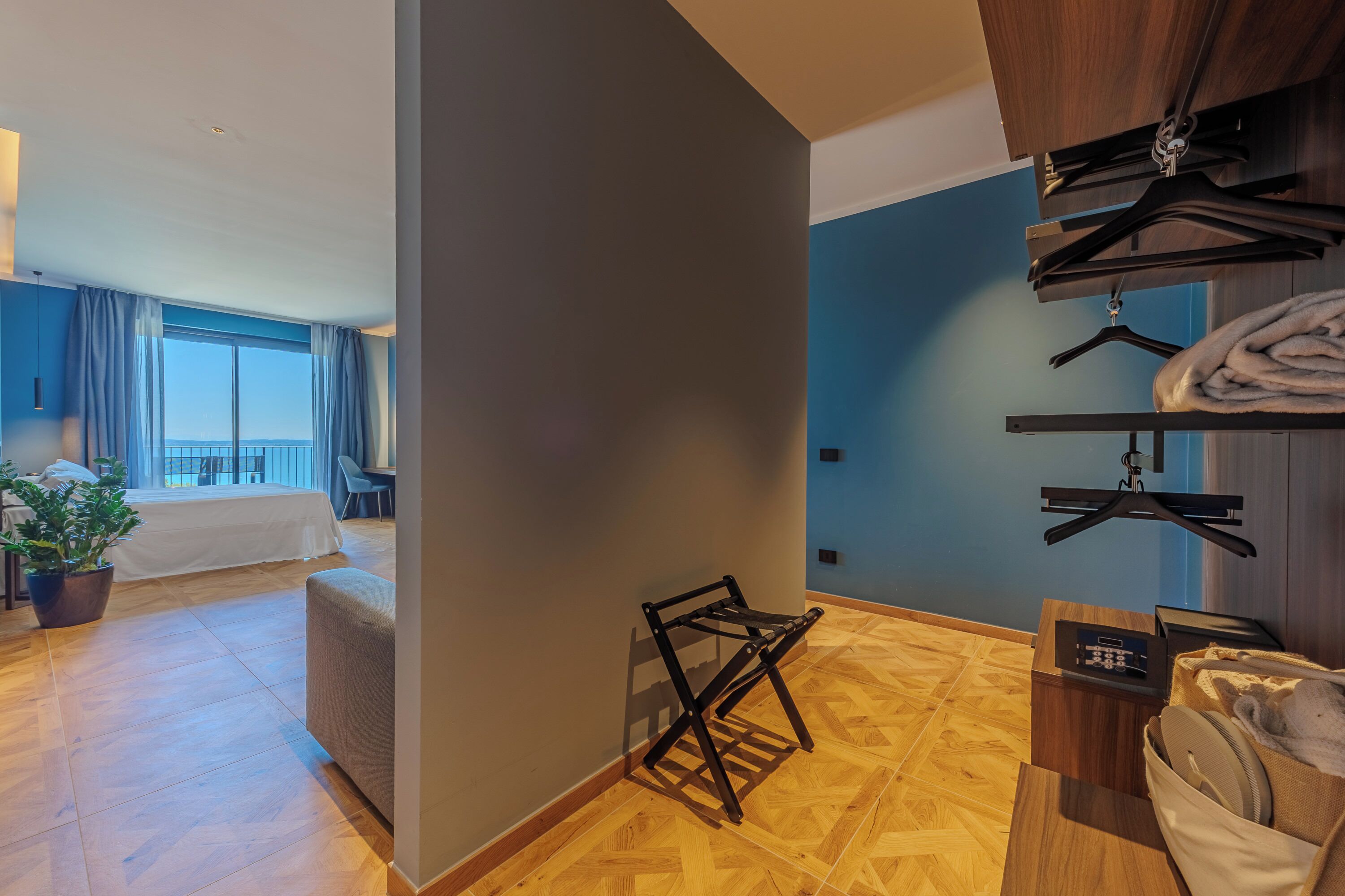 Camera d'albergo con pavimento in legno, un letto, un'area salotto, un piccolo tavolo con un telecomando e vista sull'esterno.
