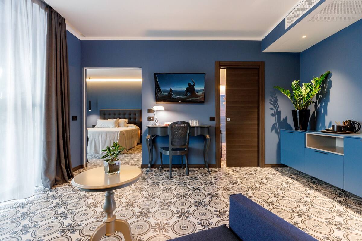 Habitación de hotel con cama, escritorio, silla, una mesita y una planta en maceta.