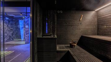Eine Sauna mit Holzbänken, einer Steinwand und einer Glastür zu einem blau beleuchteten Raum.