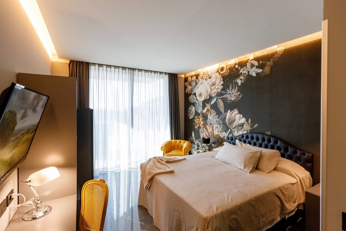 Habitación de hotel con una cama grande, un televisor de pantalla plana, un sillón amarillo y un papel tapiz floral.