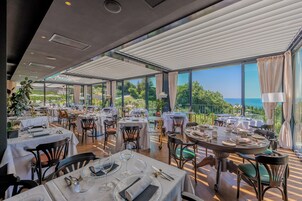 Un restaurante con mesas dispuestas para comer, amplios ventanales que ofrecen vista al mar y un techo con diseño moderno.