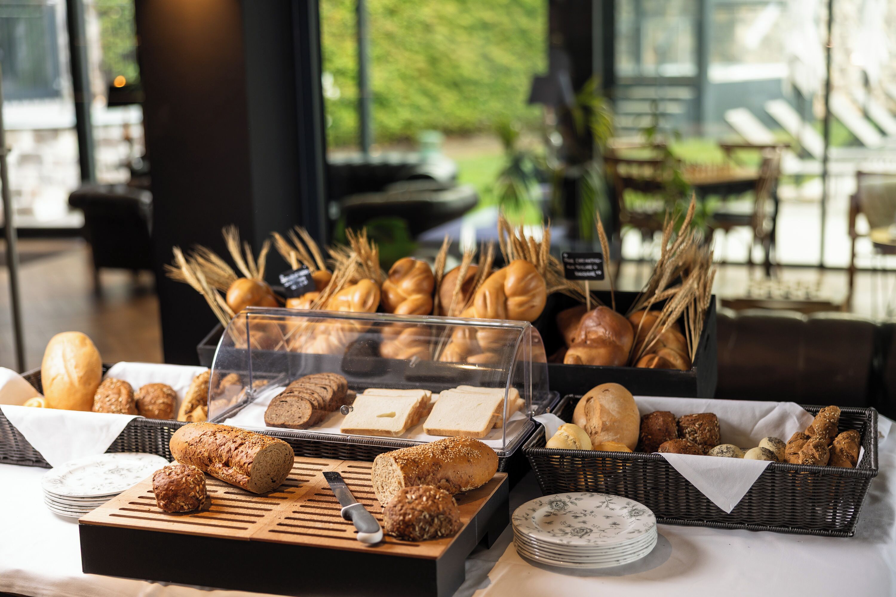Um buffet com diversos pães e doces expostos em cestas e numa tábua de madeira.