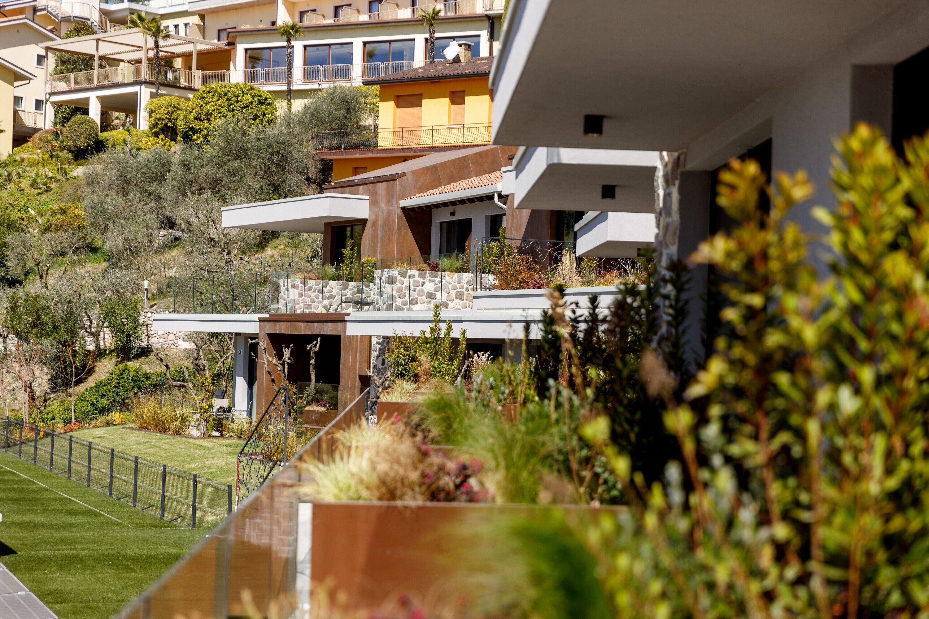 A modern residential building with a stone facade, a balcony, and a well-maintained garden.