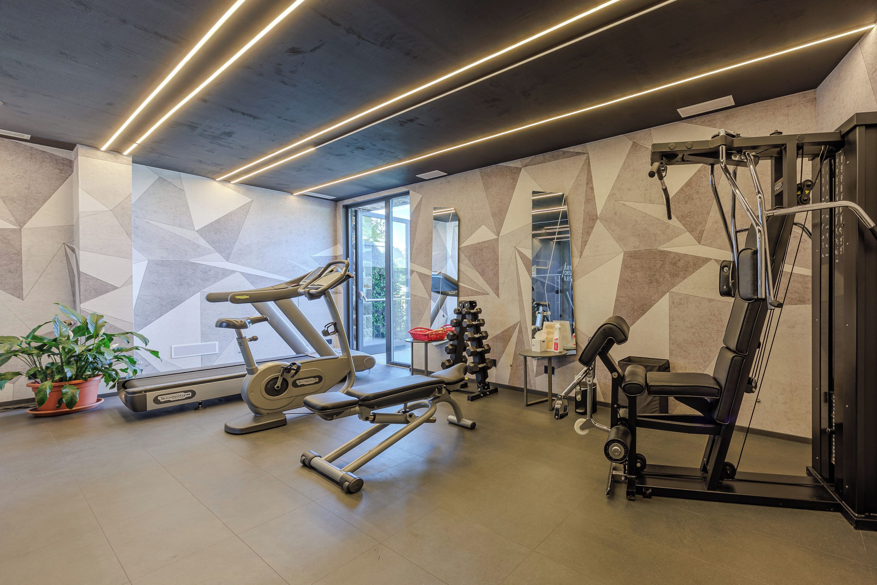 A modern gym with exercise equipment, a large window, and geometric wall patterns.