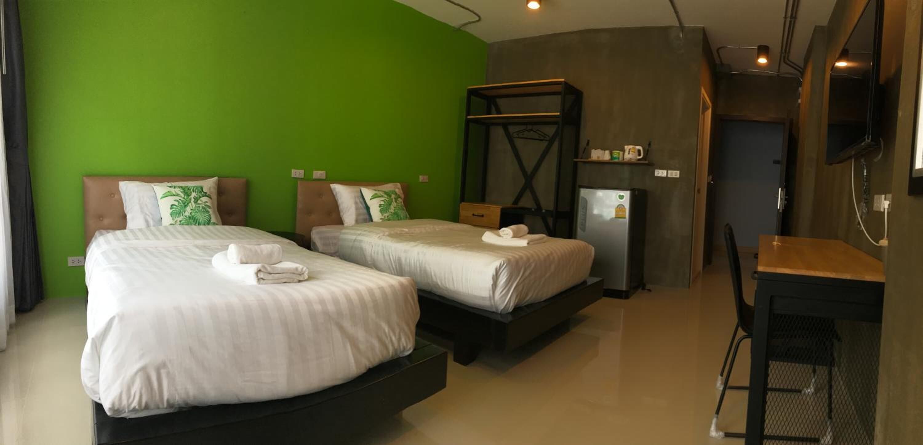 A hotel room with two beds, a desk, a chair, a TV, and a small kitchenette.