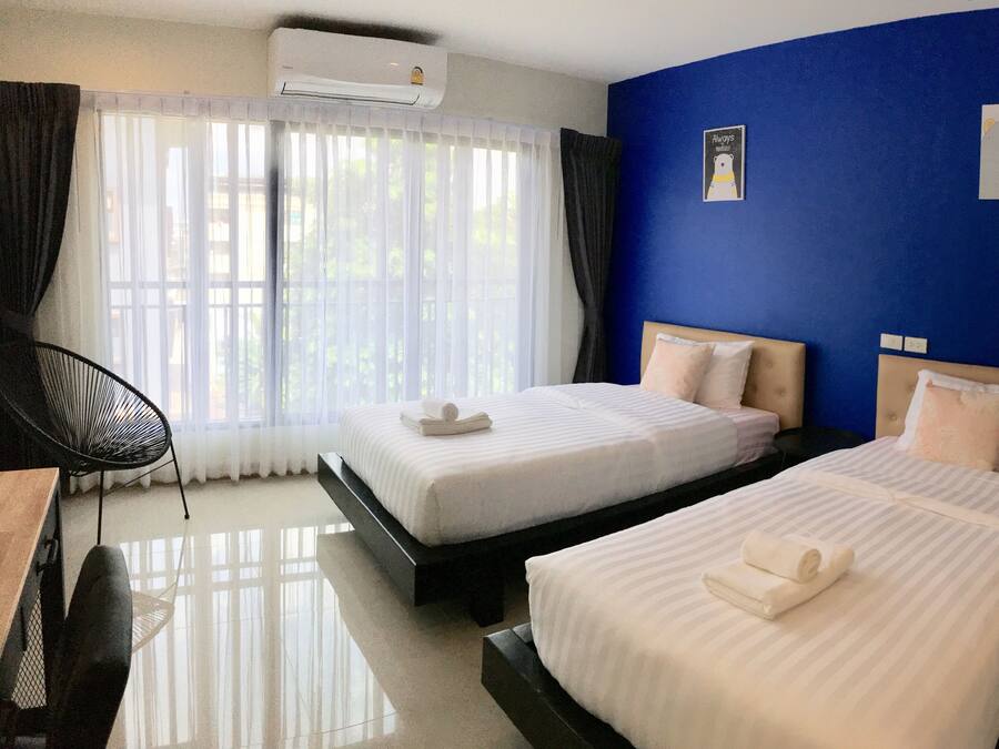 A hotel room with two beds, a desk, a chair, and a large window with curtains.