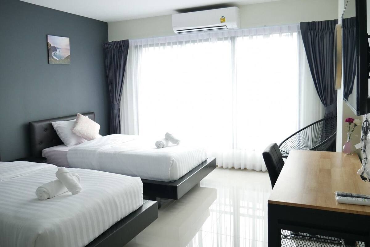 A hotel room with two beds, a desk, and a large window with curtains.