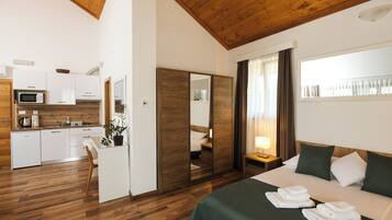 A hotel room with a bed, a bedside table, a mirror, a small kitchen area with a microwave, and a wooden ceiling.