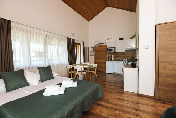 A hotel room with a bed, a dining table with chairs, a kitchen area, and wooden flooring. - B&B Apartments Buric Plitvice Lakes (Rakovica)