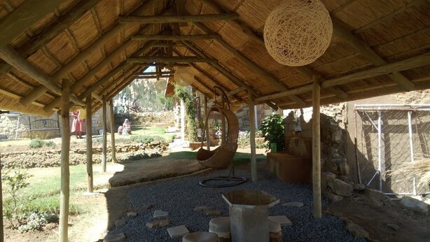 A rustic outdoor area with a thatched roof structure, stone walls, and a garden with potted plants. - Lapeng Ha Mamosa (Maseru)