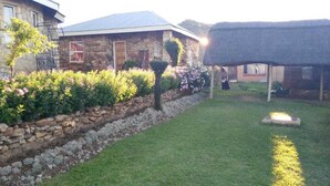 A stone house with a thatched roof structure, a stone wall with flowering plants, and a well-maintained lawn. - Lapeng Ha Mamosa (Maseru)