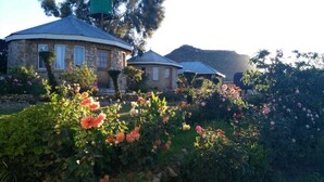 A stone building with a rounded roof, surrounded by lush gardens with various flowering plants. - Lapeng Ha Mamosa (Maseru)