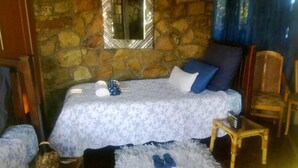 A bedroom with a stone wall, a bed with a floral bedspread, a chair, and a small table. - Lapeng Ha Mamosa (Maseru)