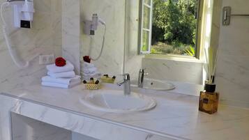 Un baño con encimera de mármol blanco, dos lavamanos, un espejo grande, un secador de pelo y una ventana con vistas a la vegetación.