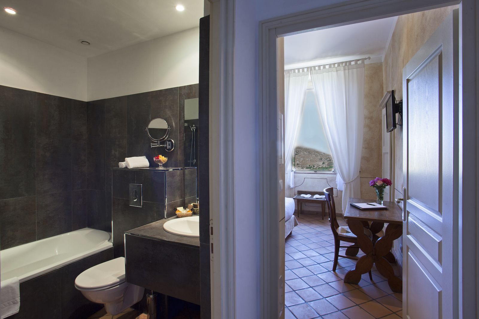 Ein modernes Badezimmer mit Badewanne, Toilette und Waschbecken. Im Balkonbereich mit Blick gibt es einen kleinen Tisch und einen Stuhl.