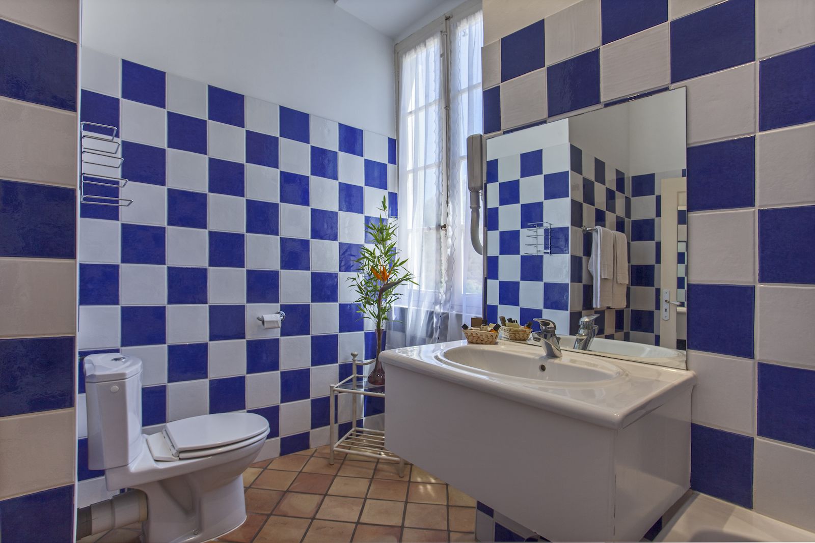 A bathroom with blue and white checkered tiles, a white sink, a mirror, and a toilet.