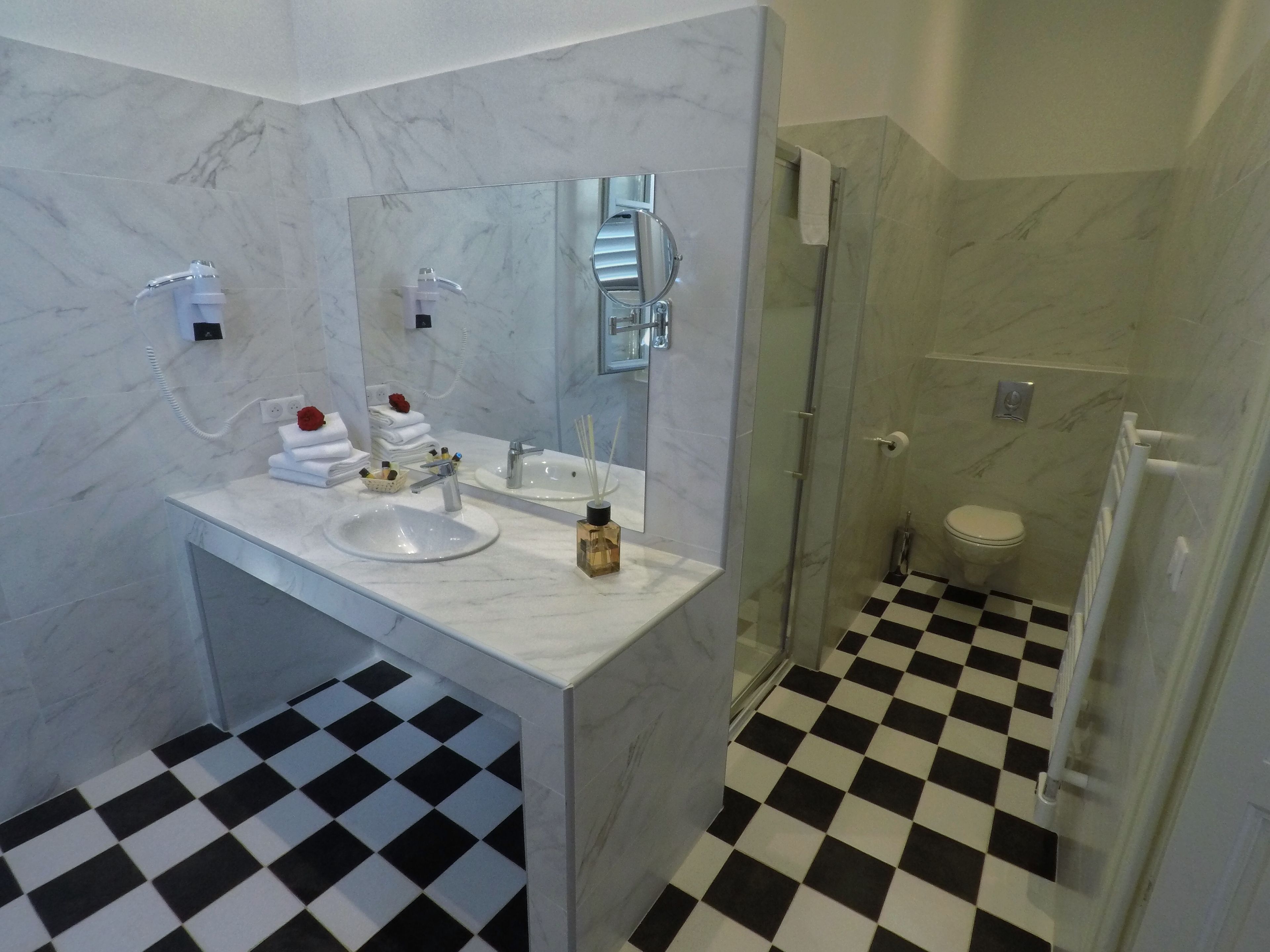 Une salle de bain avec un meuble-lavabo en marbre, un évier, un miroir, un espace douche et un carrelage à motifs carrés.