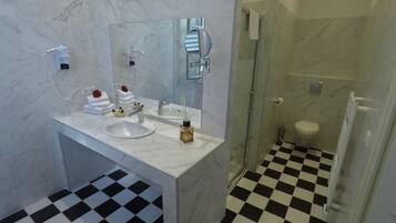 Une salle de bain avec un meuble-lavabo en marbre, un évier, un miroir, un espace douche et un carrelage à motifs carrés.