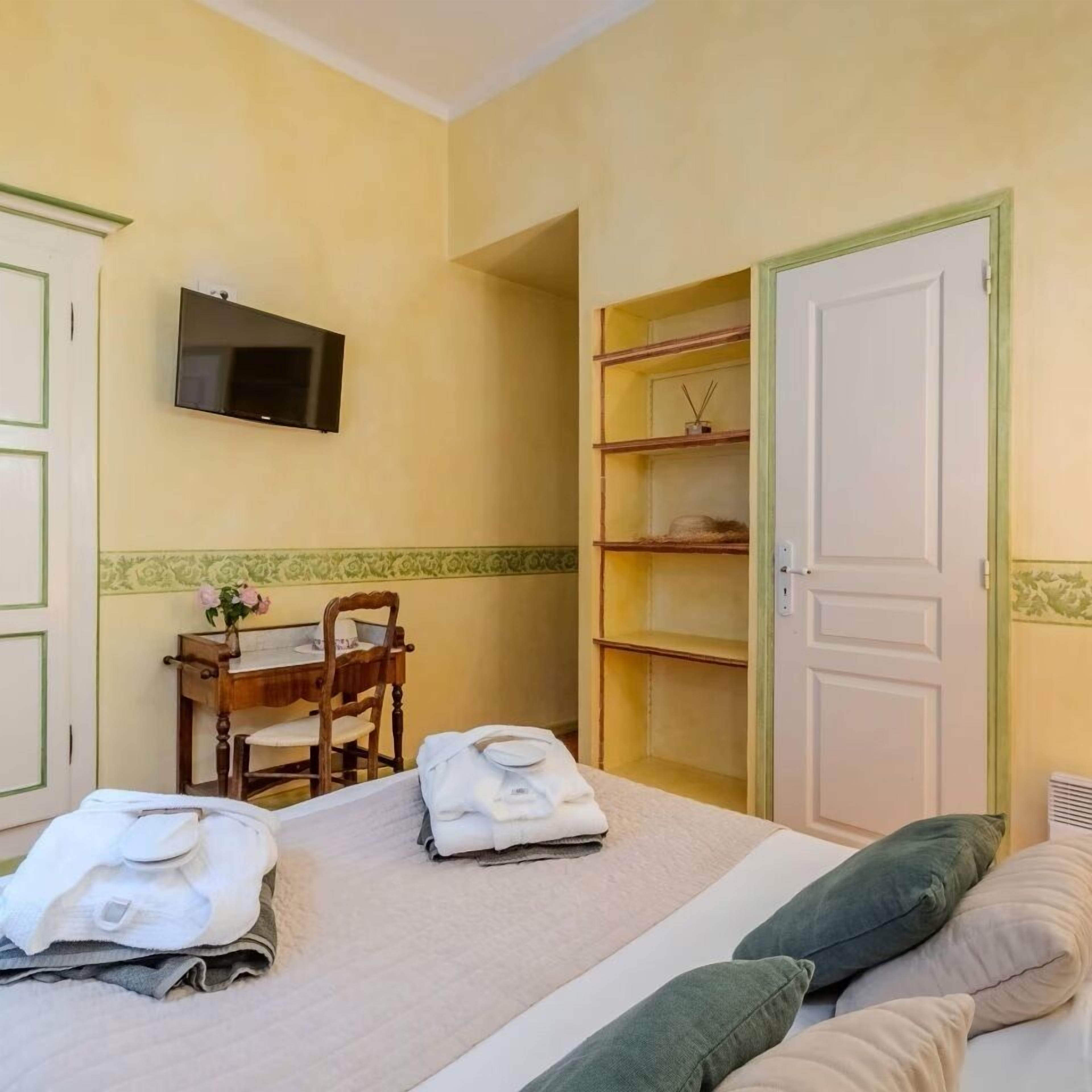 A bedroom with a bed, a desk with a chair, a TV mounted on the wall, and a wardrobe.