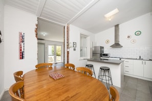 A modern kitchen with white cabinets, a stainless steel range hood, and a wooden dining table with chairs. - Central Fremantle two bedroom historic cottage (Fremantle)