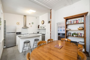 A modern kitchen with white tiles, stainless steel appliances, and a wooden dining table with chairs. - Central Fremantle two bedroom historic cottage (Fremantle)