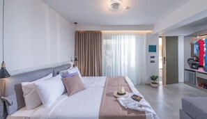 Una habitació d'hotel moderna amb un llit, una làmpada de nit, cortines, una petita planta en test i un escriptori amb mirall i portarrobes.