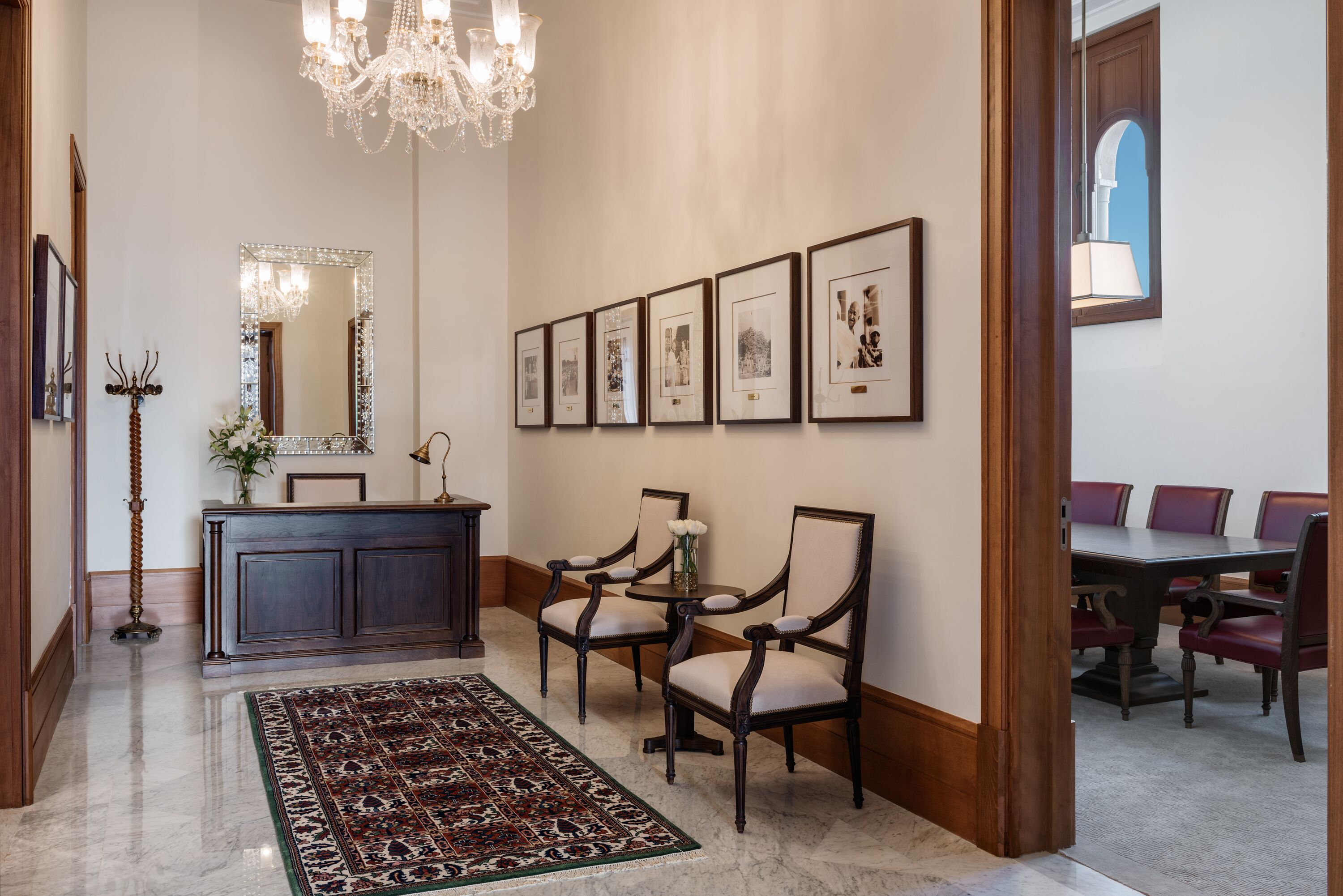 Un vestíbulo con una araña, cuadros enmarcados en la pared, una mesa de recepción y un área de comedor con sillas y una mesa.