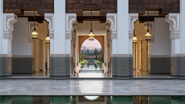 Zona de piscina con vistas a una cadena montañosa, rodeada de arcos ornamentados y azulejos estampados.