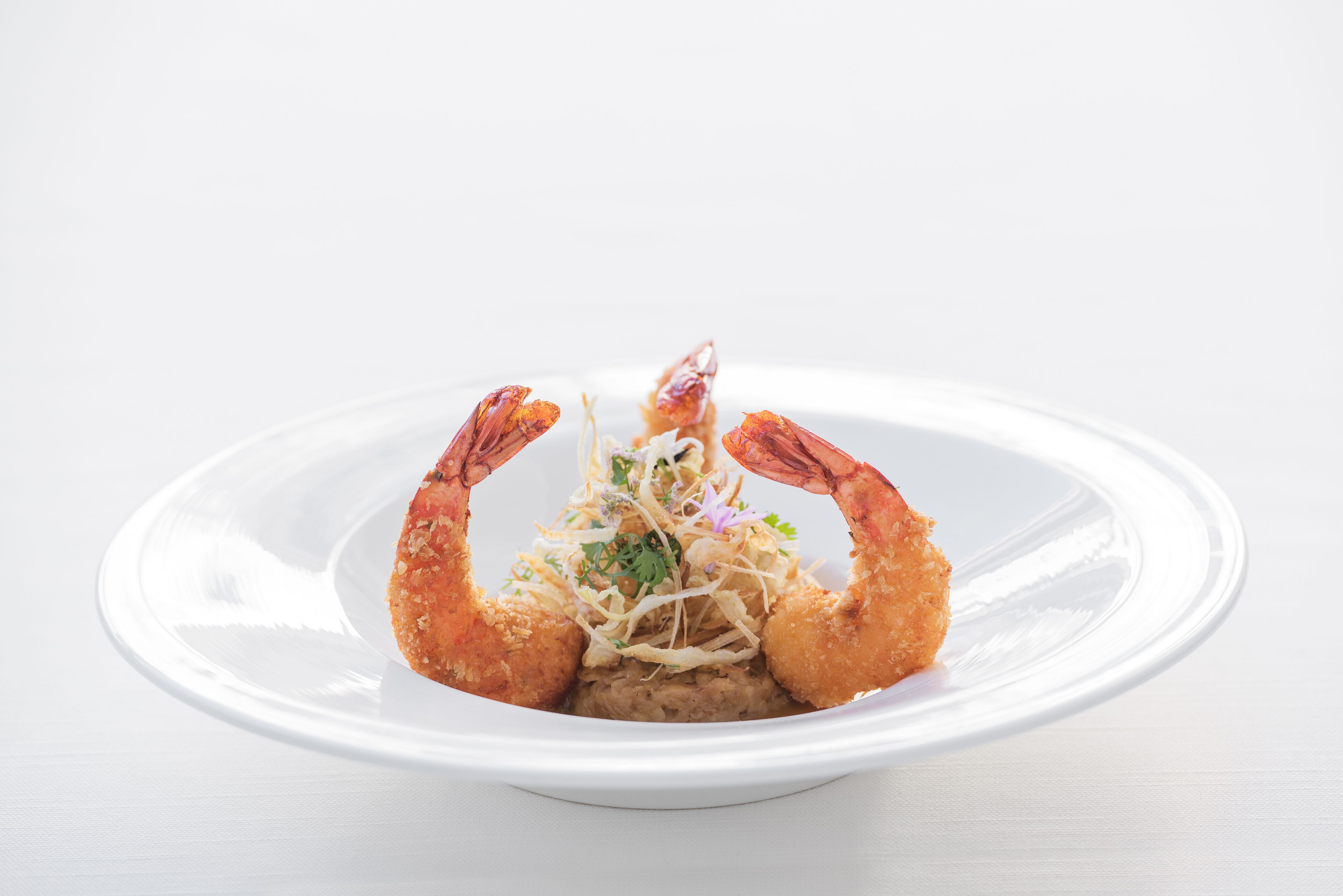 Une assiette contenant un plat composé de deux grosses crevettes, dorées et brunies, et agrémenté d’une garniture au centre.