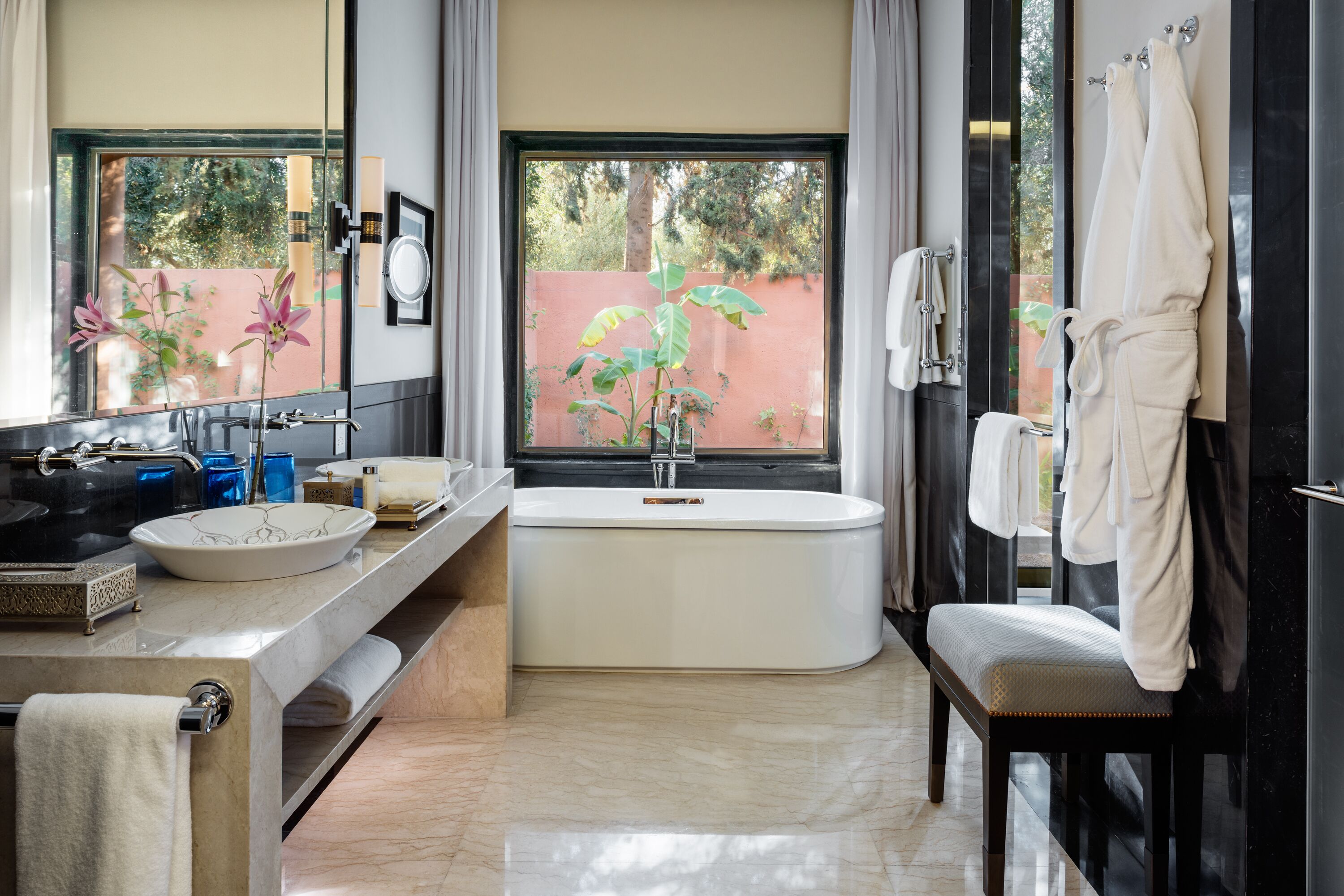A modern bathroom with a large window, a bathtub, a sink with a decorative bowl, and a bench.