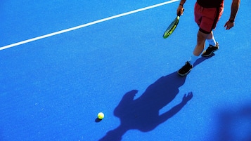 A tennis court with a shadow of a person holding a racket and a tennis ball on the ground.