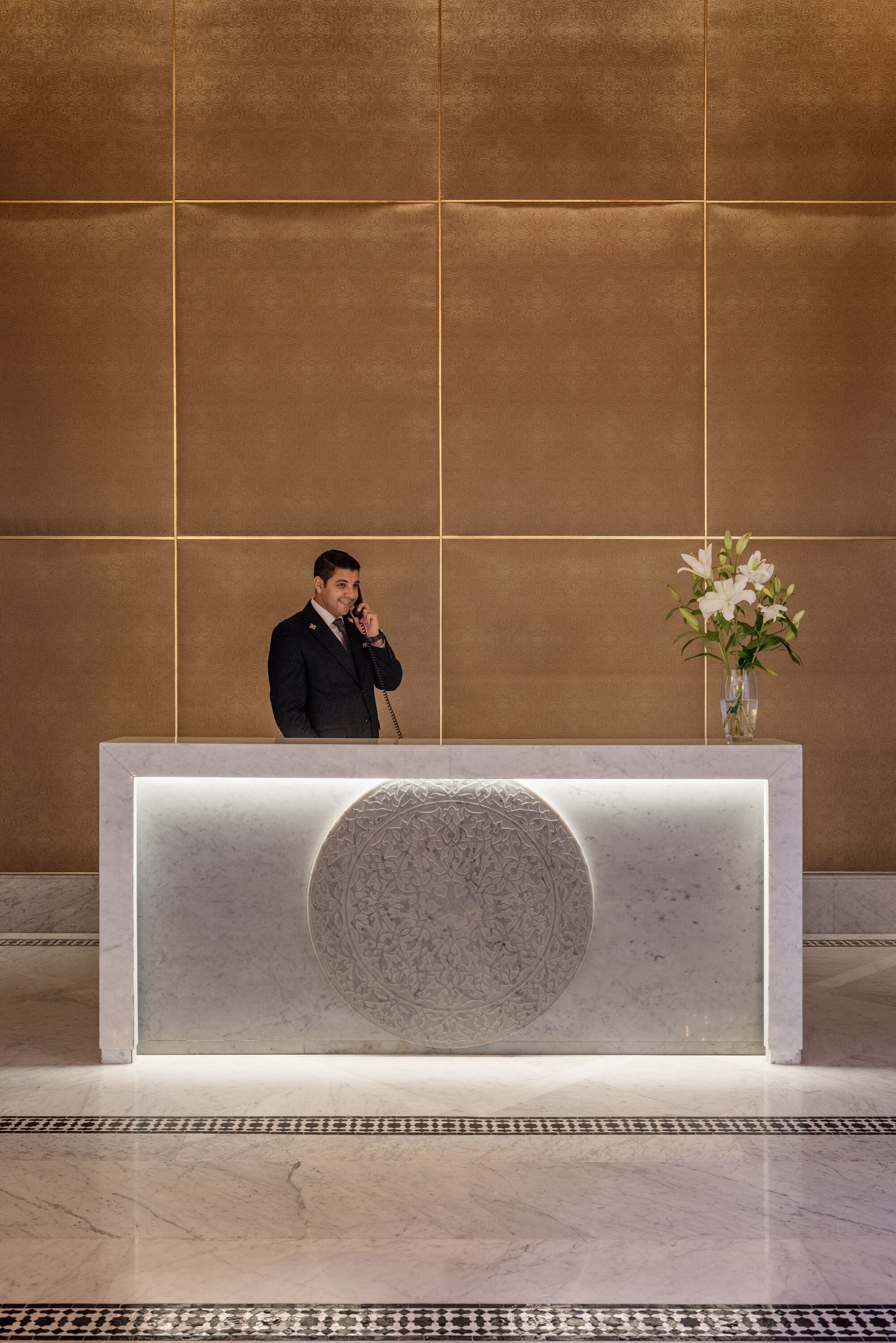 A reception desk with a marble top, a vase with flowers, and a man standing behind it.