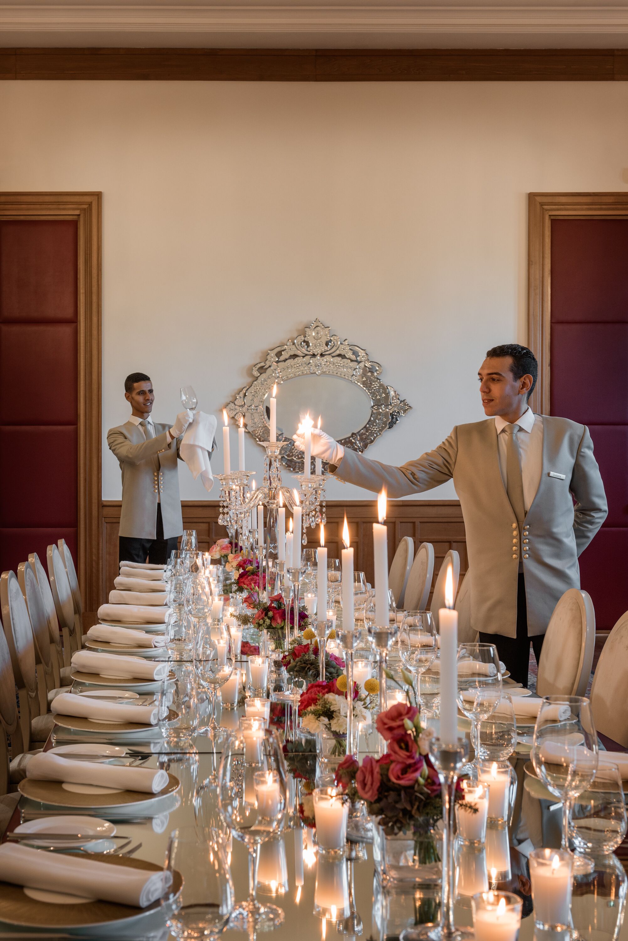 A formal dining table set with candles, flowers, and a mirror above it.
