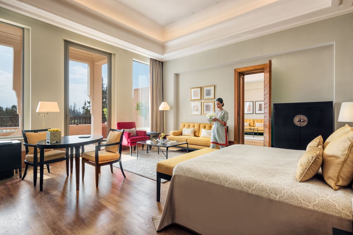 Ein Hotelzimmer mit einem großen Bett, einer Sitzecke mit Sofa und Sesseln, einem Esstisch und Blick ins Freie.