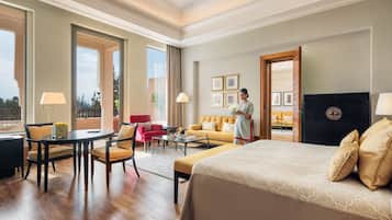 Habitación de hotel con una cama grande, una zona de estar con sofá y sillones, una mesa de comedor y vistas al exterior.
